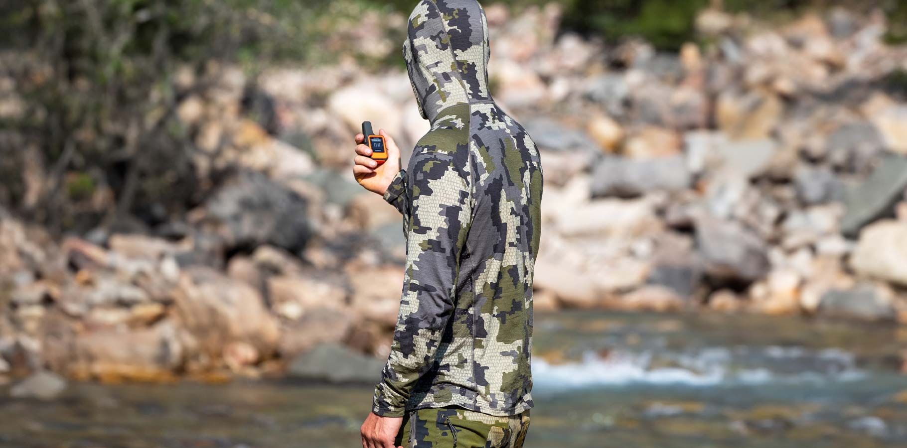 Male hunter standing in a river in head to toe KUIU Verde Camo using his Garmin inReach.