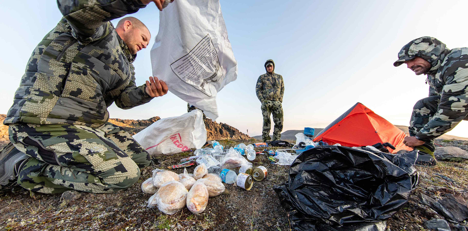 Three hunters removing pre-packaged food from their backpacks while on top of a mountain