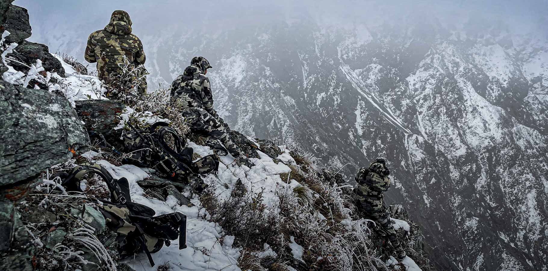 Three hunters seated on a snow covered ridge glassing for mountain goats