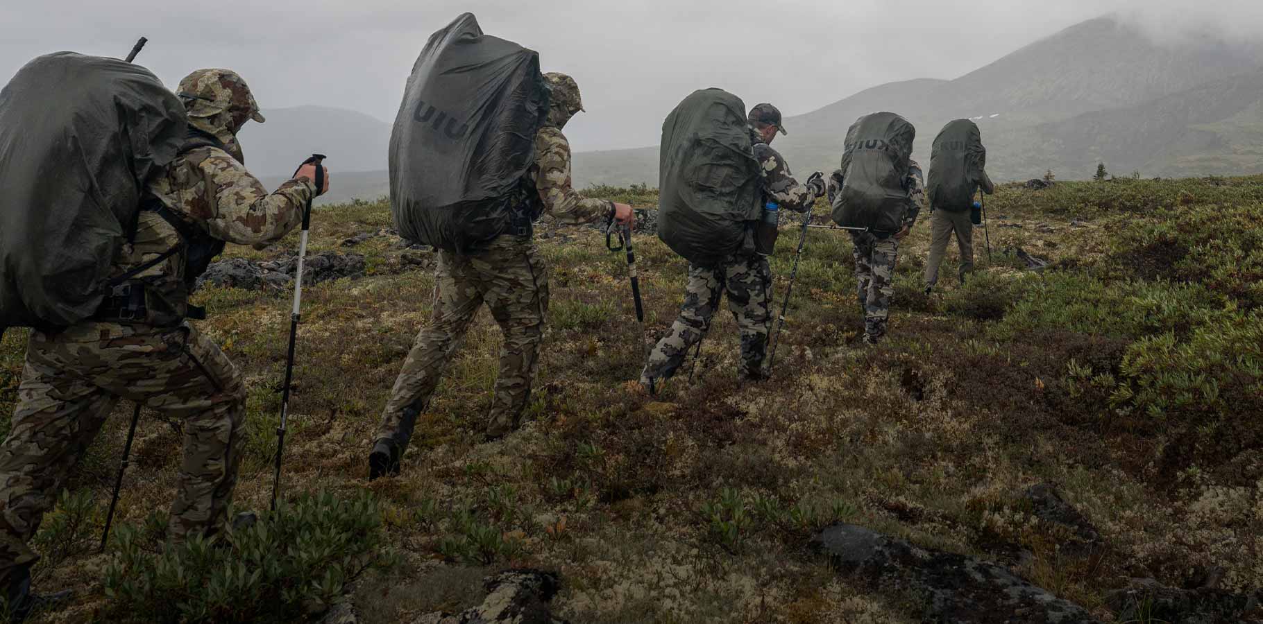 Five hunters walking in a single file line while wearing covered packs during a heavy rain storm