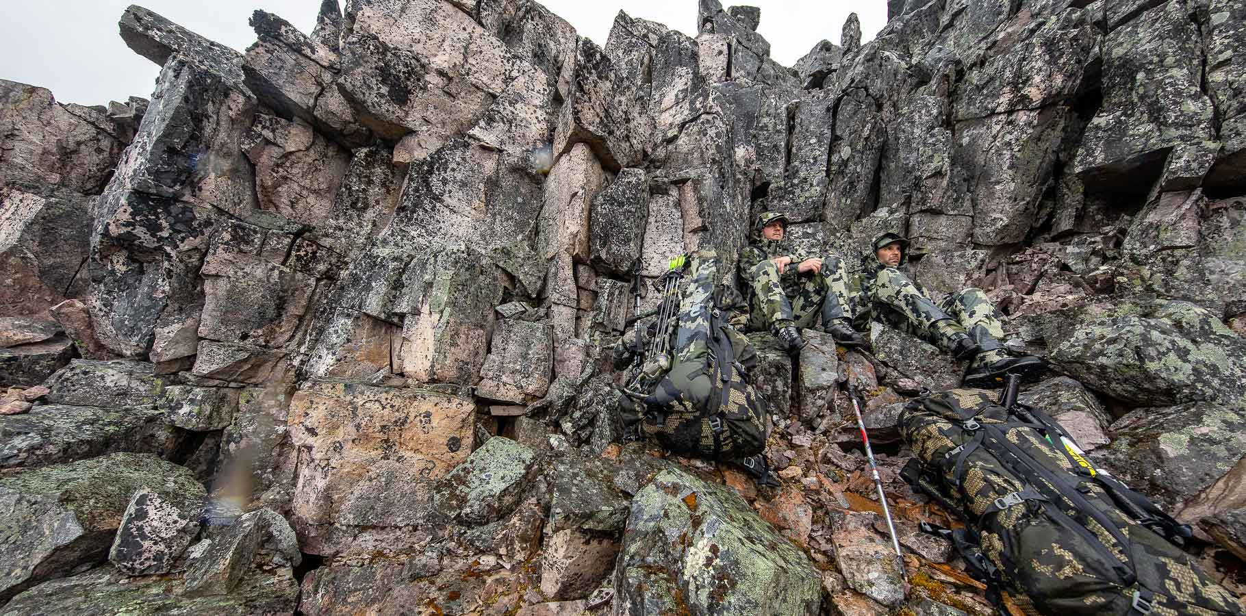 Front of Hunters Wearing Kutana Storm Shell Jackets in Verde Camouflage Tucked Against Rock Face