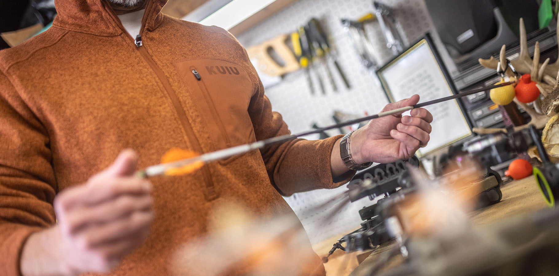 Male checking the spine stiffness of his carbon fiber arrow while wearing an orange hued fleece pullover