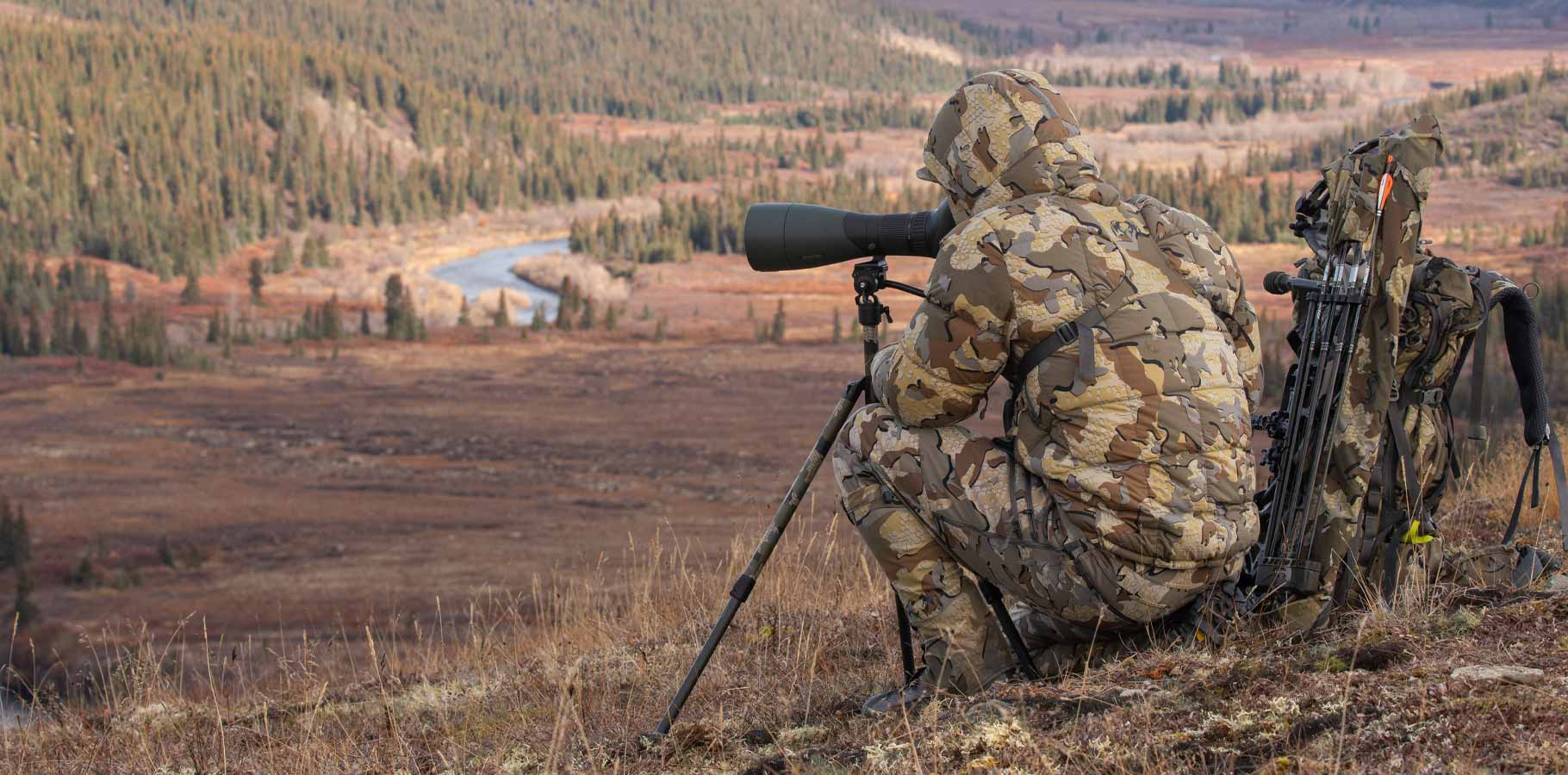 Hunter in Super Down PRO Hooded Jacket in Valo Camouflage looking through spotting scope