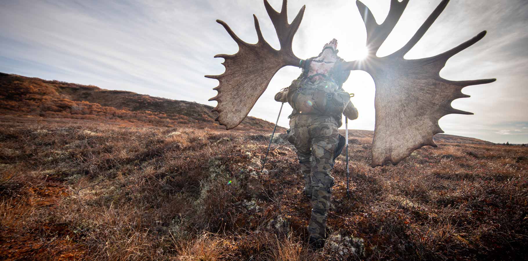 Brendan Burns in Valo camouflage carrying out the cleaned skull of his Alaskan moose uphill and back to the plane