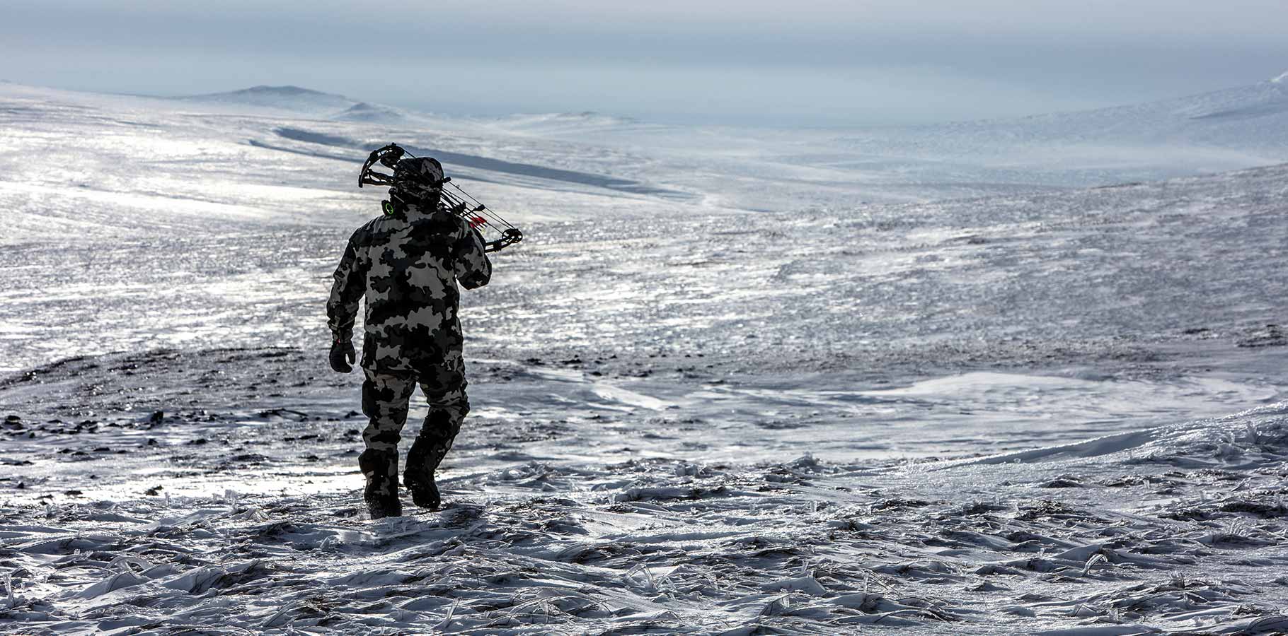 Back of Hunter Hiking With Bow Wearing Vias Camouflage in Snowy Tundra