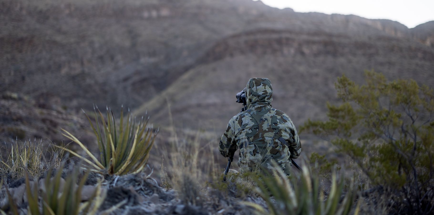 Hunter in Valo Camouflage looking through binoculares while faced away from the camera