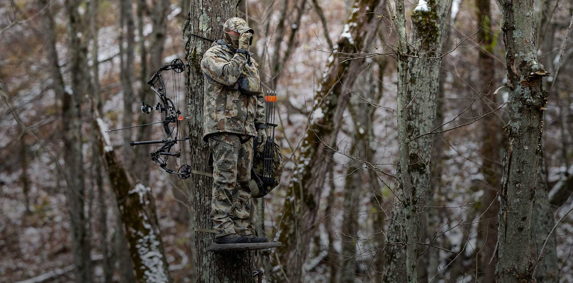 Hunter in valo camouflage standing in a tree stand using his rangefinder to determine his distance to target