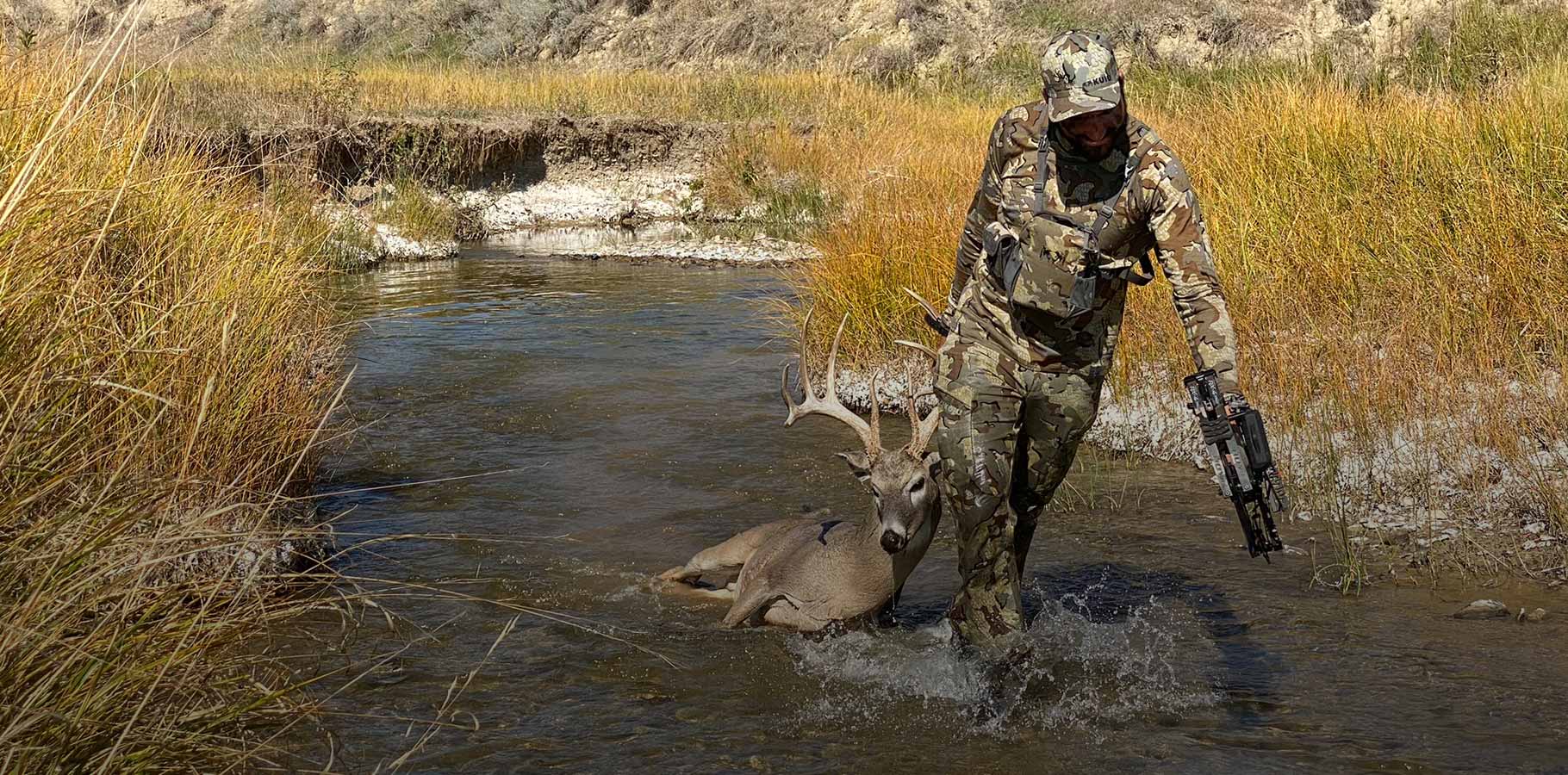 AJ Kissel wearing Valo camouflage as he drags a mature whitetail buck through the creek