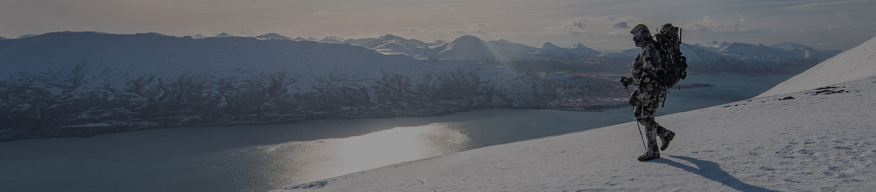 Hunter trekking through the snow with a breathtaking view of a mountain range and river winding below