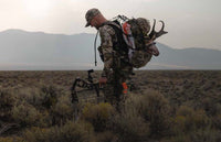 Hunter in Valo camouflage walking out with pronghorn buck skull and cape packed into backpack