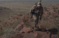 Hunter in valo camouflage hiking uphill along a rocky desert spine in Mexico
