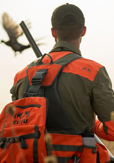 Upland hunter wearing Sporter Shirt in Major Brown/Blaze Orange and the Upland Field Vest in Blaze Orange with pheasant flying in close proximity