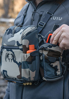 PRO Chest Pack shown in Vias Camouflage with hunter placing GPS device in side accessory pocket