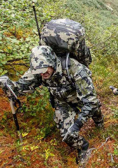 Front, Angled View of Hunter Wearing Verde Camouflage Hiking Up Thick, Wet, Green Hill