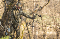 Bow Hunter camouflaged in the tree stand aiming his bow and arrow ready to shoot