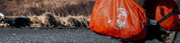 Side of Hunter Carrying Taku 5500 Duffels in Blaze Orange Color on Rocky Beach